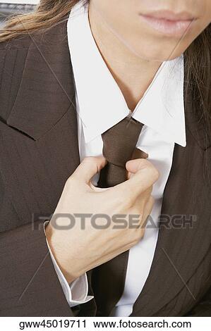 Stock Image - Mid section view of a businesswoman adjusting her tie. Fotosearch