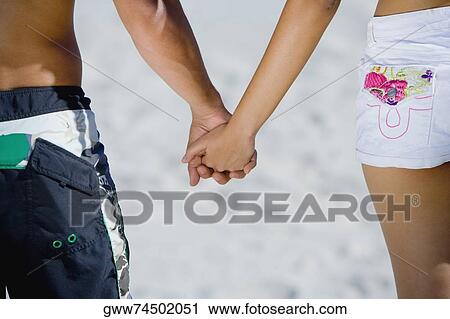 Mid section view of a couple holding hands View Large Photo Image Stock Image - Mid section view of a couple holding hands. Fotosearch