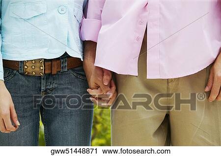 Stock Image - Mid section view of a man and woman standing and holding hands. Fotosearch
