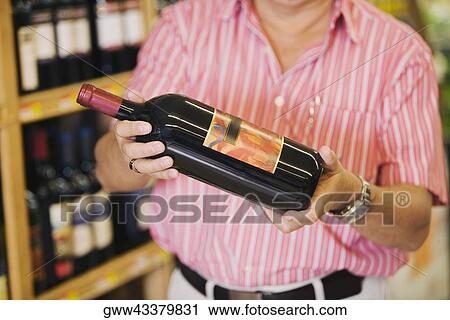 Mid section view of a man holding a wine bottle in a liquor store View Large Photo Image Stock Image - Mid section view of a man holding a wine bottle in a liquor store. Fotosearch