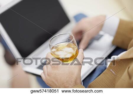 Stock Image - Mid section view of a man using a laptop and holding a glass of wine. Fotosearch