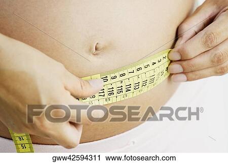 Mid section view of a pregnant woman measuring her abdomen with a tape measure View Large Photo Image Stock Image - Mid section view of a pregnant woman measuring her abdomen with a tape measure. Fotosearch