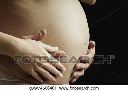 Mid section view of a pregnant woman touching her abdomen View Large Photo Image Stock Image - Mid section view of a pregnant woman touching her abdomen. Fotosearch