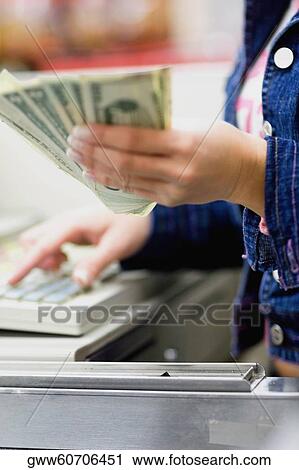 Stock Image - Mid section view of a sales clerk holding paper currency in a checkout counter. Fotosearch