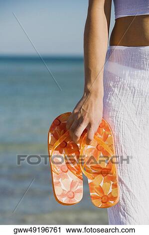 Mid section view of a woman holding a pair of flip-flops on the beach View Large Photo Image Stock Image - Mid section view of a woman holding a pair of flip-flops on the beach. Fotosearch