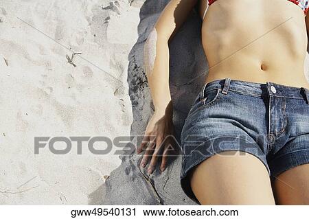 Stock Image - Mid section view of a woman lying on the beach. Fotosearch
