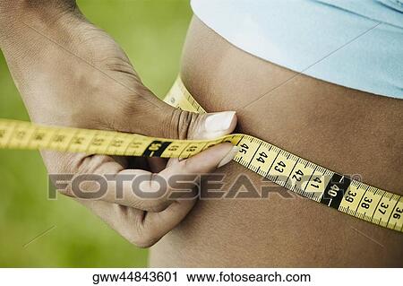 Mid section view of a woman measuring her waist with a tape measure View Large Photo Image Stock Image - Mid section view of a woman measuring her waist with a tape measure. Fotosearch