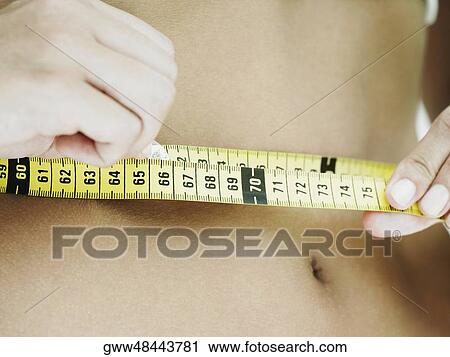 Mid section view of a woman measuring her waist with a tape measure View Large Photo Image Stock Image - Mid section view of a woman measuring her waist with a tape measure. Fotosearch