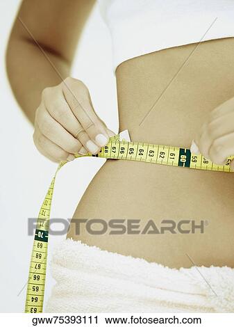Mid section view of a woman measuring her waist with a tape measure View Large Photo Image Stock Image - Mid section view of a woman measuring her waist with a tape measure. Fotosearch