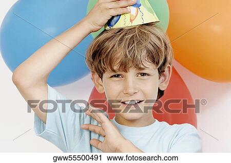 Stock Image - Portrait of a boy holding party hat on his head. Fotosearch