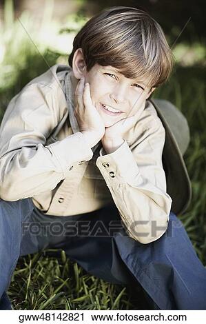 Stock Image - Portrait of a boy sitting with his hands on his chin and smiling. Fotosearch