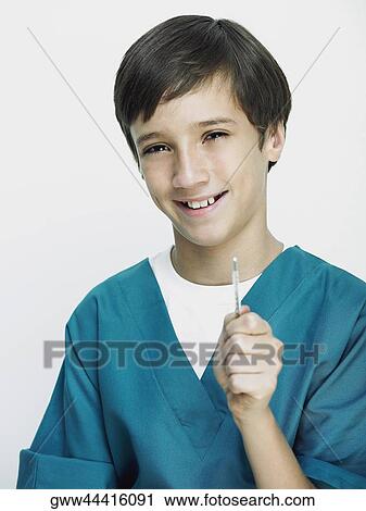 Stock Image - Portrait of a boy wearing surgical scrubs and holding a thermometer. Fotosearch