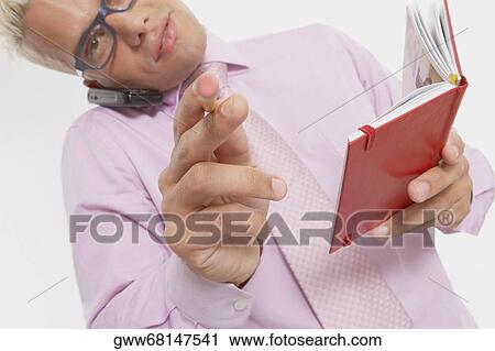 Stock Image - Portrait of a businessman talking on a mobile phone and pointing with a pencil. Fotosearch
