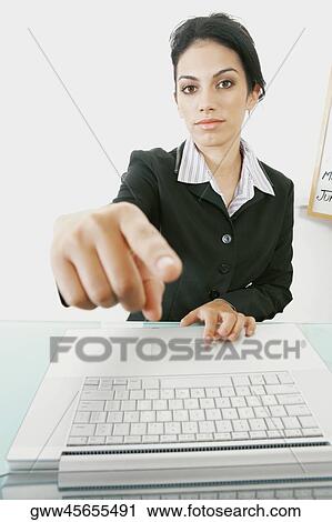 Portrait of a businesswoman sitting in front of a laptop and pointing forward View Large Photo Image Stock Image - Portrait of a businesswoman sitting in front of a laptop and pointing forward. Fotosearch