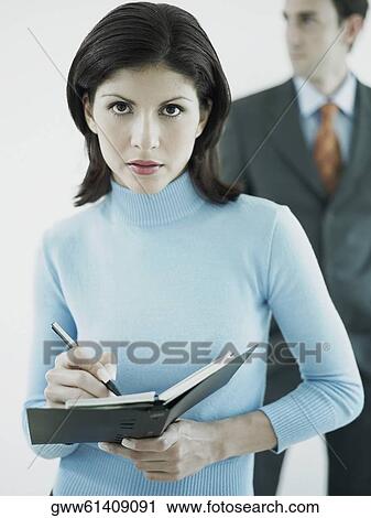 Portrait of a businesswoman writing on a personal organizer with a businessman standing behind her View Large Photo Image Stock Image - Portrait of a businesswoman writing on a personal organizer with a businessman standing behind her. Fotosearch