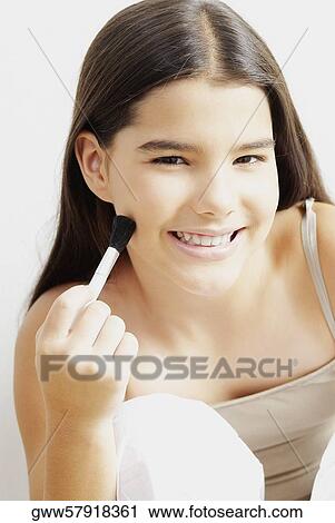 Stock Image - Portrait of a girl applying make-up on her face. Fotosearch