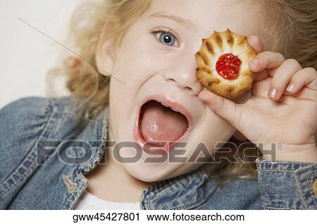 Stock Image - Portrait of a girl covering her one eye with a biscuit. Fotosearch