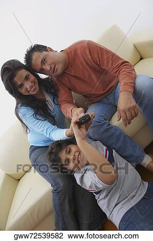 Stock Image - Portrait of a mid adult man and a young woman with their son watching television. Fotosearch
