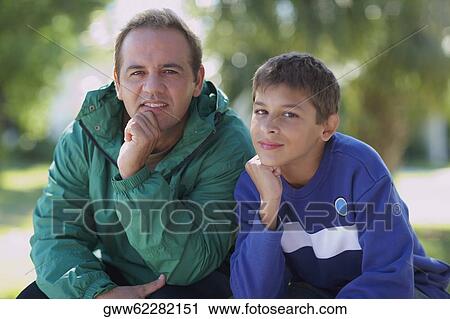 Portrait of a mid adult man and his son sitting with their hand on chin View Large Photo Image Stock Image - Portrait of a mid adult man and his son sitting with their hand on chin. Fotosearch