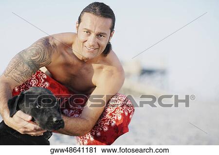 Portrait of a mid adult man crouching on the beach with a dog and smiling View Large Photo Image Stock Image - Portrait of a mid adult man crouching on the beach with a dog and smiling. Fotosearch