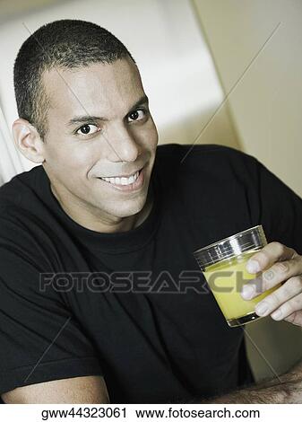 Stock Image - Portrait of a mid adult man holding a glass of orange juice and smiling. Fotosearch