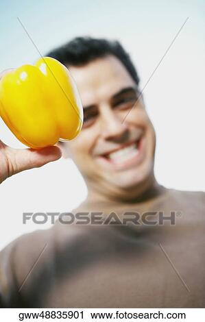 Stock Image - Portrait of a mid adult man holding a yellow bell pepper. Fotosearch