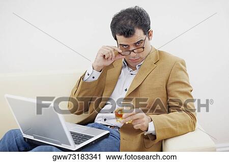 Stock Image - Portrait of a mid adult man holding a glass of wine and looking over his eyeglasses. Fotosearch