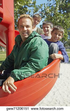 Stock Image - Portrait of a mid adult man on a slide with his three children. Fotosearch