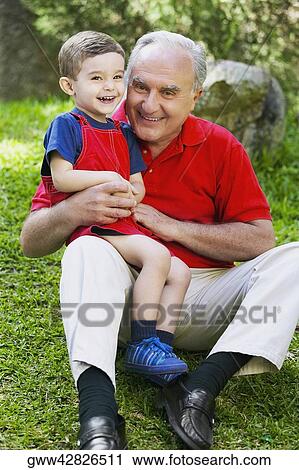 Stock Image - Portrait of a senior man sitting with his grandson smiling. Fotosearch