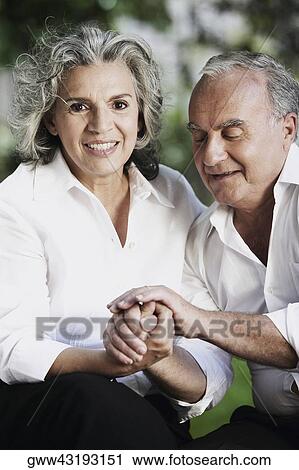 Stock Image - Portrait of a senior woman smiling with a senior man holding her hands. Fotosearch