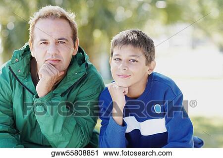 Portrait of a teenage boy and his father sitting with their hands on their chins View Large Photo Image Stock Image - Portrait of a teenage boy and his father sitting with their hands on their chins. Fotosearch