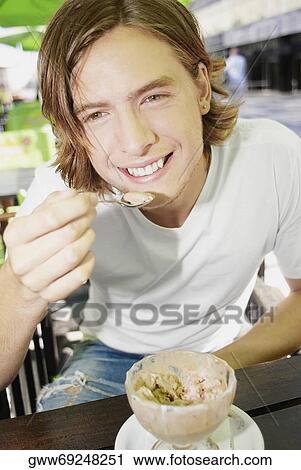 Stock Image - Portrait of a teenage boy eating an ice-cream sundae and smiling. Fotosearch
