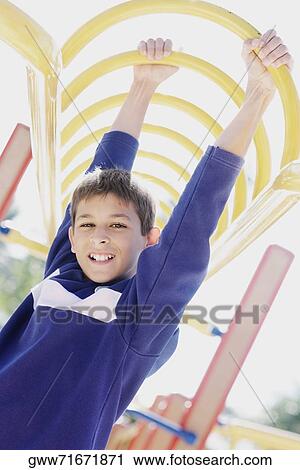 Stock Image - Portrait of a teenage boy hanging on monkey bars. Fotosearch