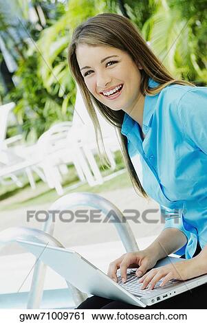 Stock Image - Portrait of a teenage girl using a laptop and smiling. Fotosearch