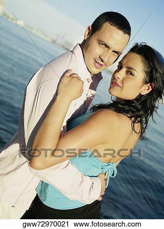 Stock Image - Portrait of a young couple standing on the beach. Fotosearch