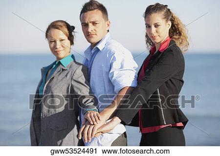 Stock Image - Portrait of a young man and two young women standing with their hands one on the top of other. Fotosearch