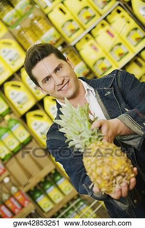 Portrait of a young man holding a pineapple in a supermarket View Large Photo Image Stock Image - Portrait of a young man holding a pineapple in a supermarket. Fotosearch