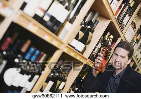 Portrait of a young man holding a wine bottle in a supermarket View Large Photo Image Stock Image - Portrait of a young man holding a wine bottle in a supermarket. Fotosearch