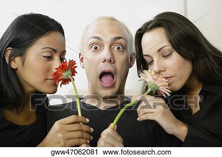 Stock Image - Portrait of a young man holding flowers with two young women smelling them. Fotosearch