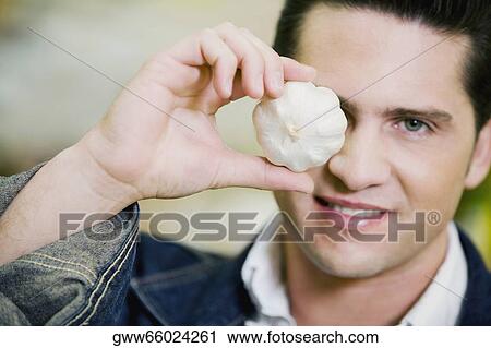 Stock Image - Portrait of a young man holding garlic. Fotosearch