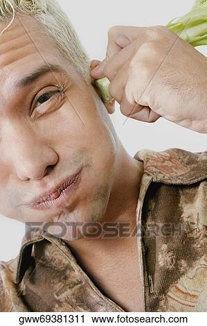 Stock Image - Portrait of a young man holding broccoli on his ears. Fotosearch