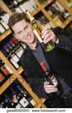 Portrait of a young man showing a wine bottle in a liquor store View Large Photo Image Stock Image - Portrait of a young man showing a wine bottle in a liquor store. Fotosearch
