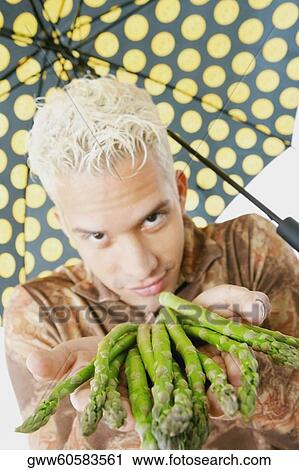 Stock Image - Portrait of a young man showing asparagus. Fotosearch