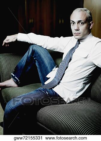 Stock Image - Portrait of a young man sitting on a couch. Fotosearch