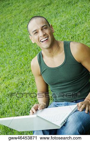 Portrait of a young man sitting with a laptop on his lap and smiling View Large Photo Image Stock Image - Portrait of a young man sitting with a laptop on his lap and smiling. Fotosearch