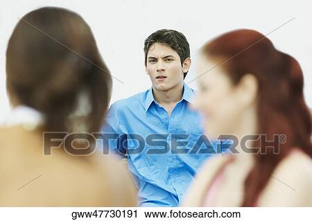 Stock Image - Portrait of a young man sitting with two young women. Fotosearch
