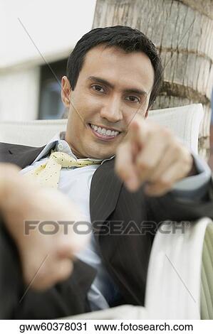 Stock Image - Portrait of a young man smiling and pointing forward. Fotosearch