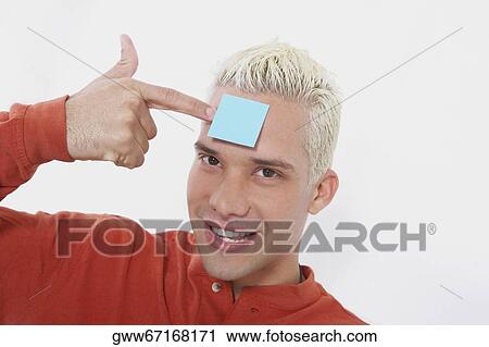 Stock Image - Portrait of a young man smiling with an adhesive note on his forehead. Fotosearch