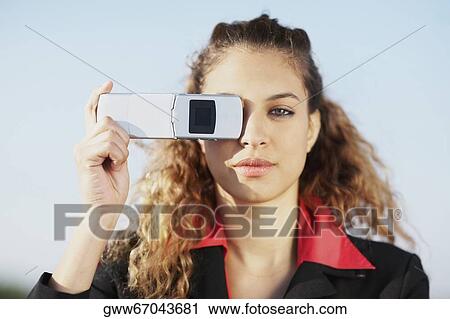 Portrait of a young woman covering her eye with a mobile phone View Large Photo Image Stock Image - Portrait of a young woman covering her eye with a mobile phone. Fotosearch