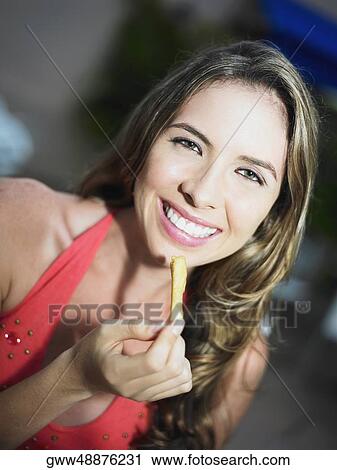 Stock Image - Portrait of a young woman eating French fries. Fotosearch